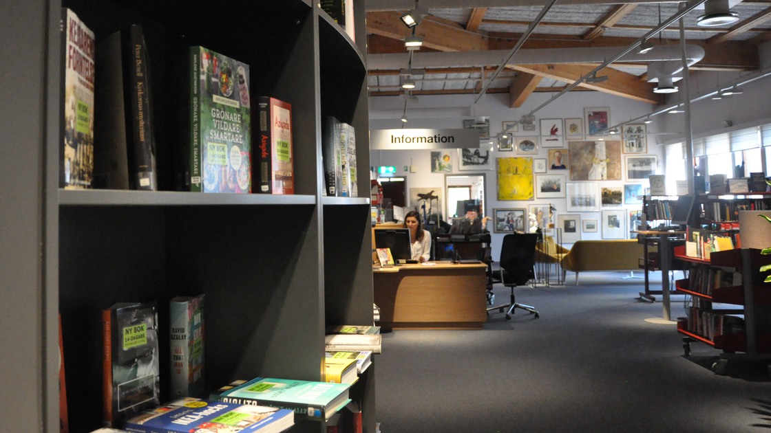 Miljöbild bibliotek. Vänster i bild bokhylla med böcker. Längre fram i bild informationsdisk.