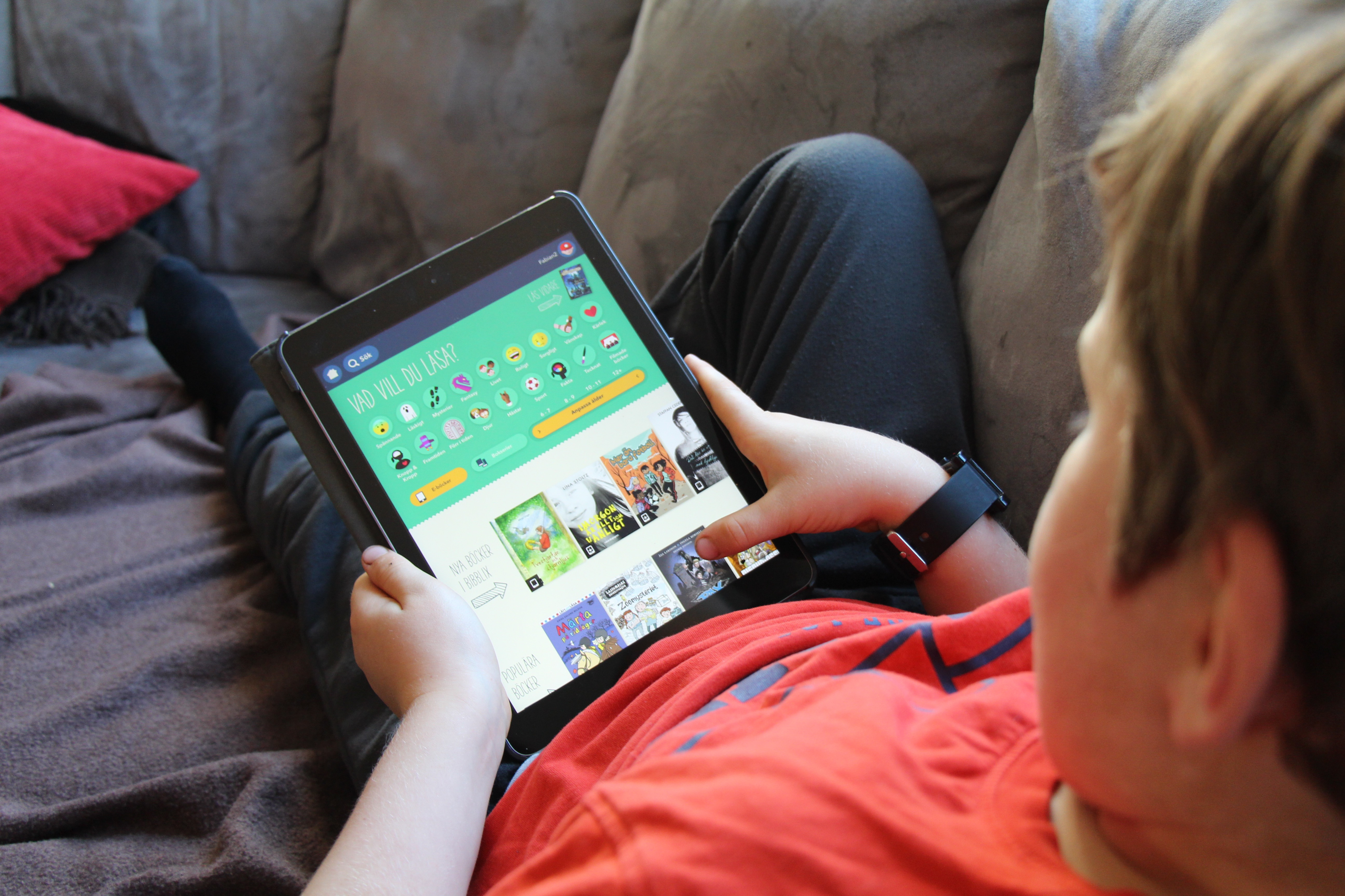 Ett barn sitter i en soffa, hållandes en  Ipad med appen Bibblix.