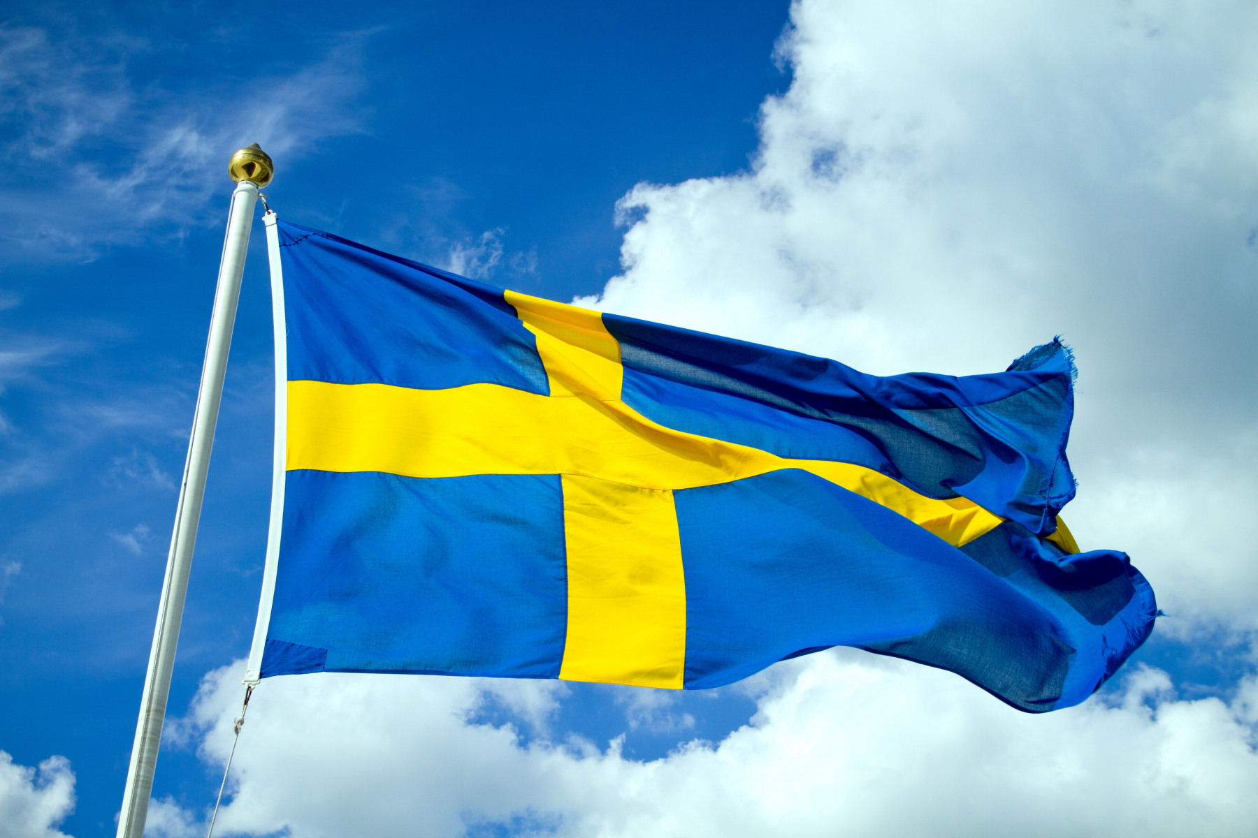Svenska flaggan fladdrar i vinden med himlen som bakgrund.