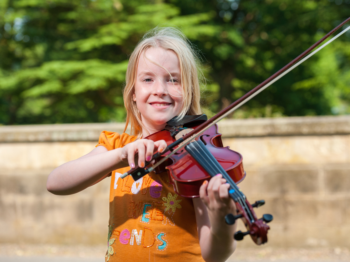 Happy young blonde girl playing violin outdoors