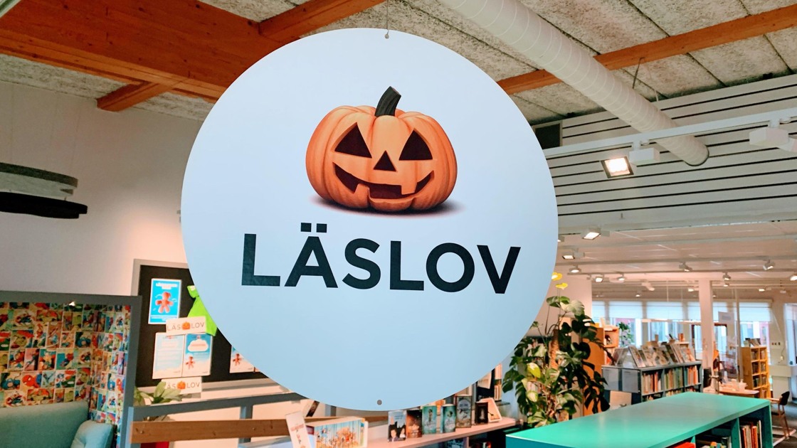 Hängande rund vit skylt med pumpa och text Läslov, I bakgrunden bokhyllor.