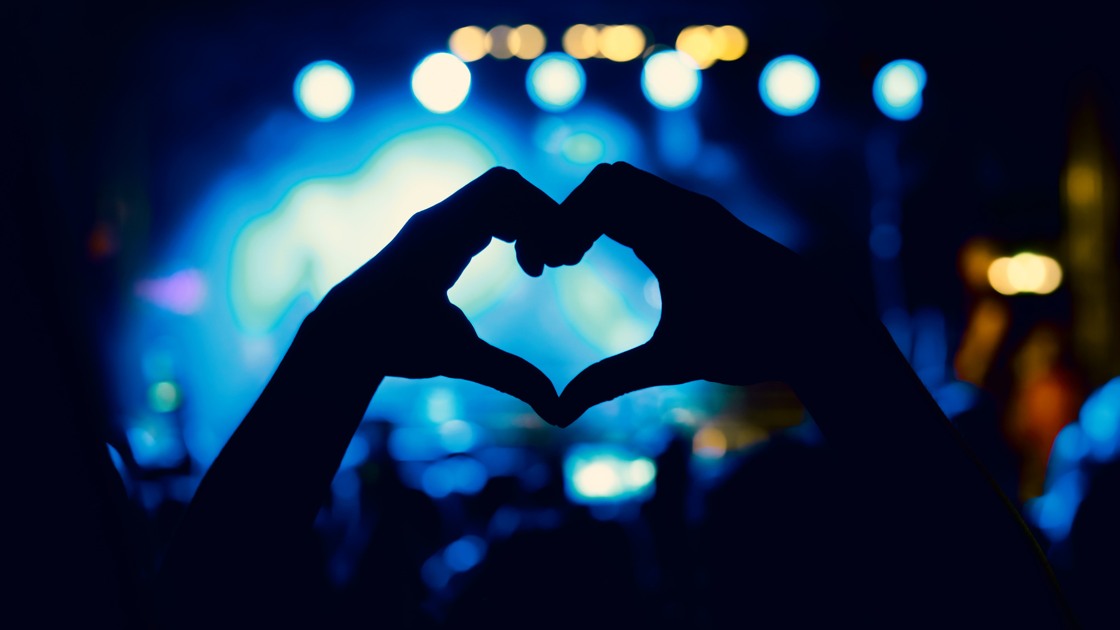 Händer som formar ett hjärta framför en scen.