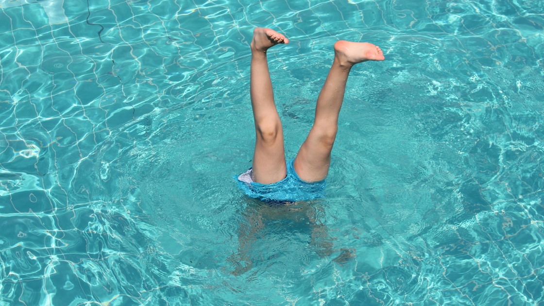 Pojke som står på händer i en pool.