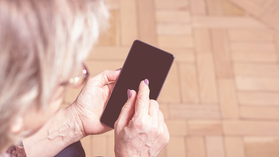 Äldre kvinna håller i en smartphone.