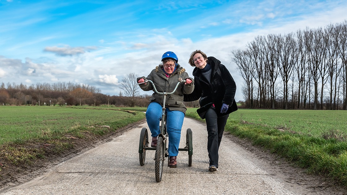 Person med funktionsnedsättning som cyklar på en trehjuling tillsammans med en ledsagare.