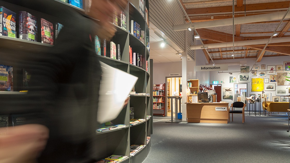 Miljöbild från biblioteket. Vänster i bild bokhylla med böcker. Längre fram informationsdisk.