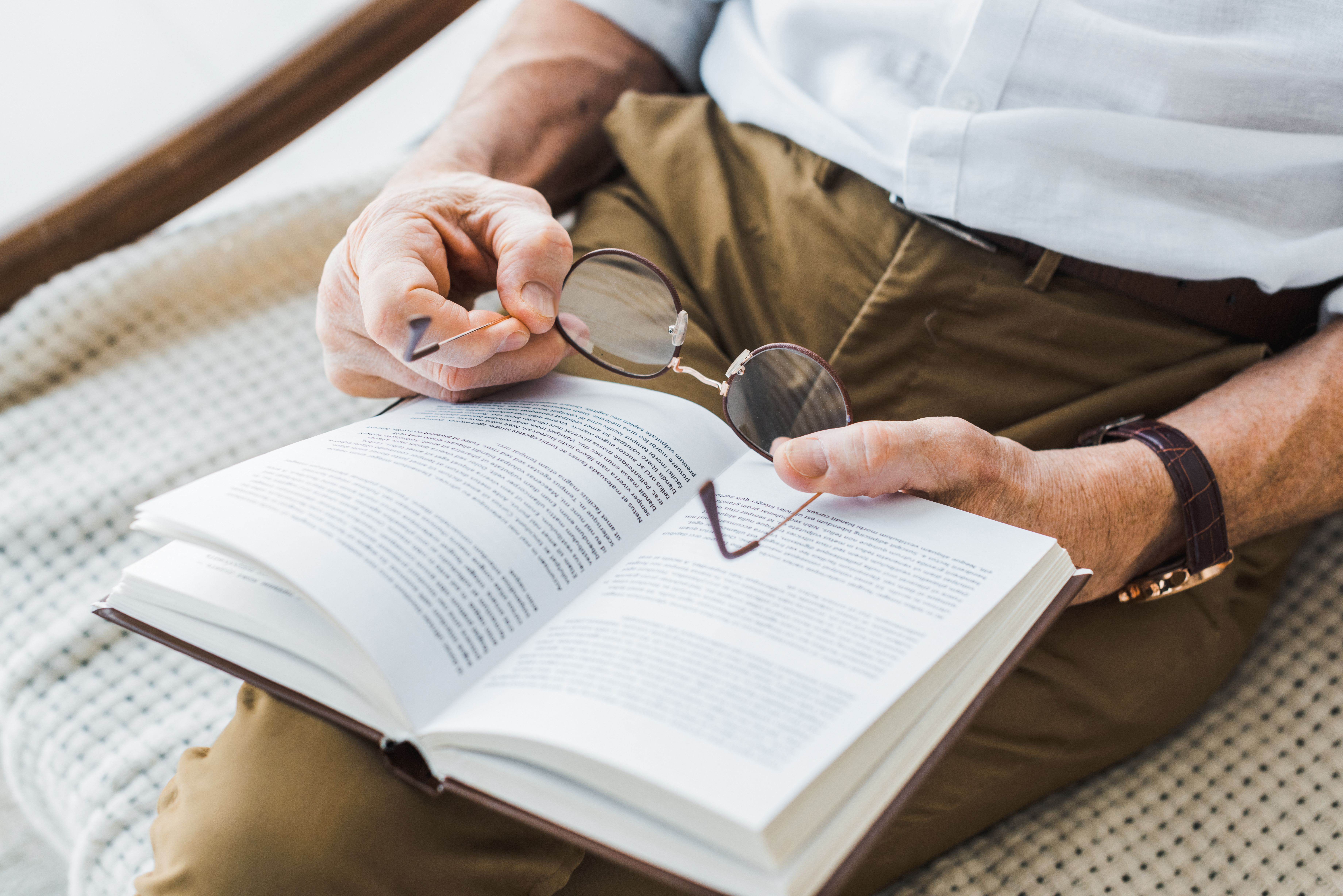 cropped view of senior man reading book and holding glasses at home