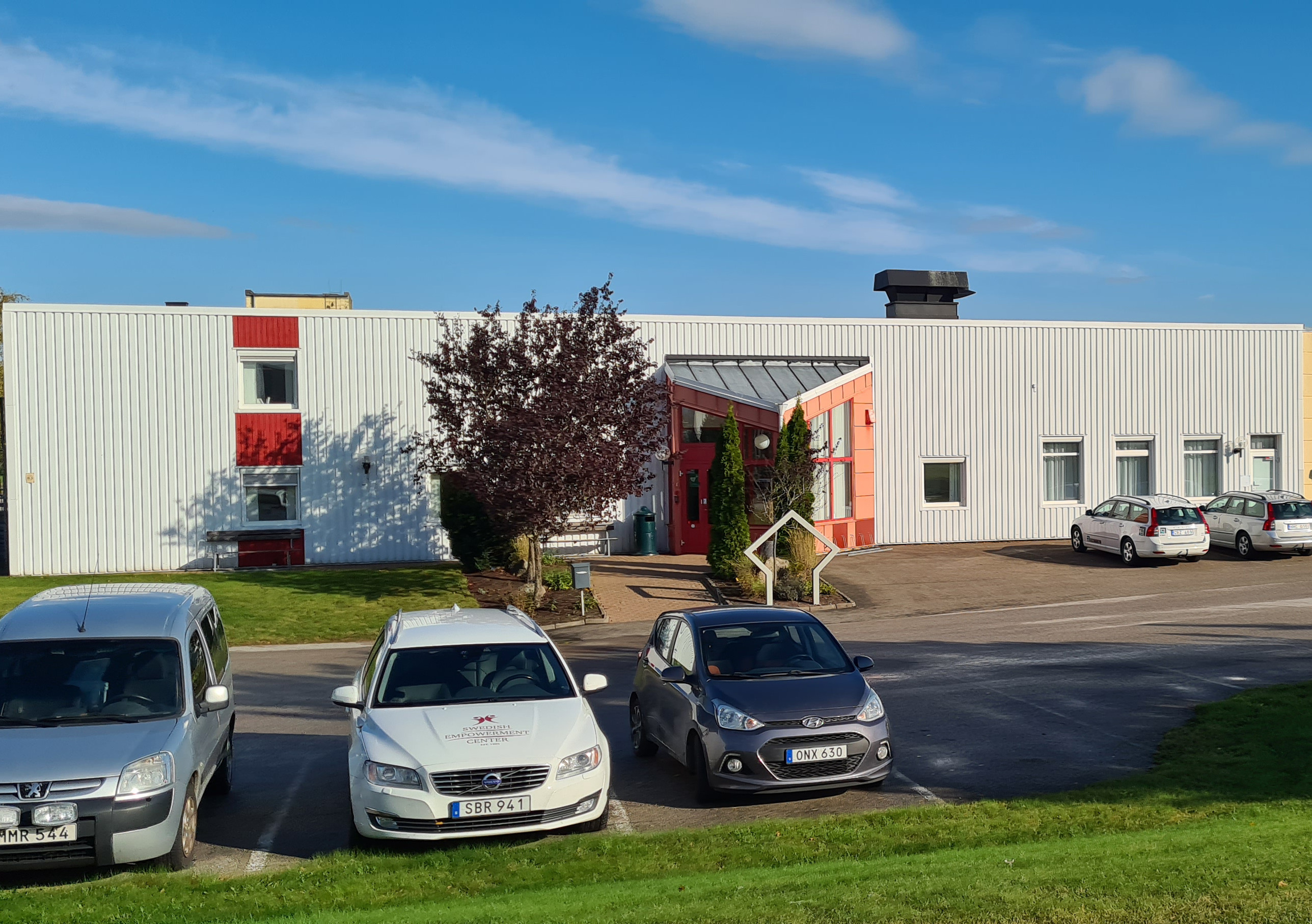 En grupp bilar som står parkerade på en parkeringsplats intill en byggnad.