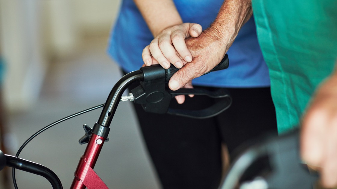 Sjuksköterska, äldre patient och händer med rullator för pension, hemtjänst och stöd eller välbefinnande. Medicinsk hjälp, fysioterapi och rehabilitering efter skada samt person med funktionsnedsättning i lounge.