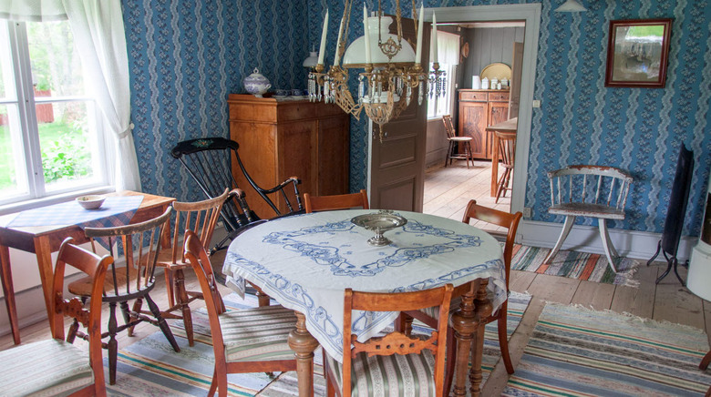 Ett av hembygdsgårdens rum med vackra gamla bord och stolar, blå tapeter en ljuskrona hängandes över ena bordet.