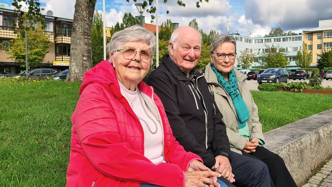 Två äldre kvinnor och en äldre man sitter på en bänk.