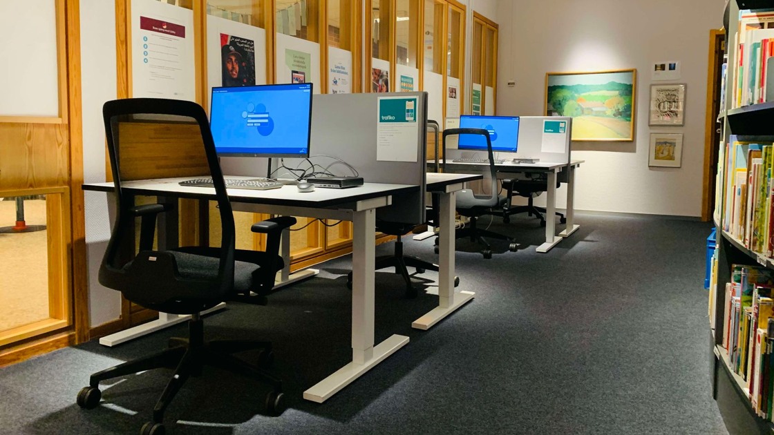 Bild från biblioteket. Längs en fönstervägg står fyra skrivbord på rad med stol och datorskärm vid varje plats.