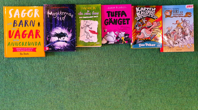 Barnböcker i olika storlekar och färger ligger på en rad mot grön bakgrund.