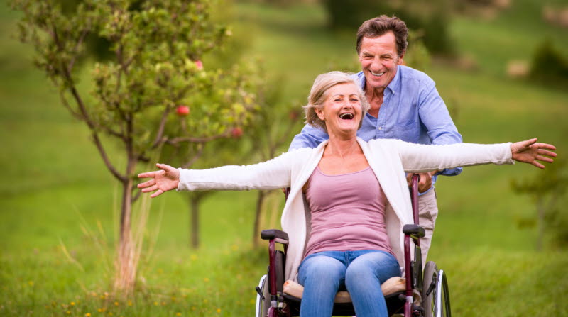 Lycklig man och kvinna på promenad med rullstol.