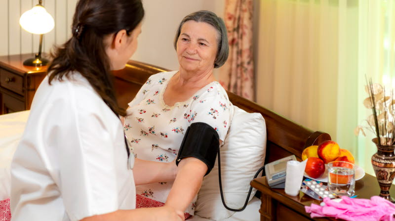Omvårdnadspersonal som tar blodtryck på äldre kvinna
