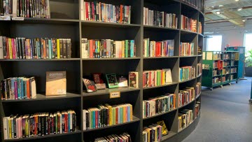 Stor grå bokhylla fylld av böcker i blandade färder. Till höger i bild skymtar ytterligare en bokhylla.