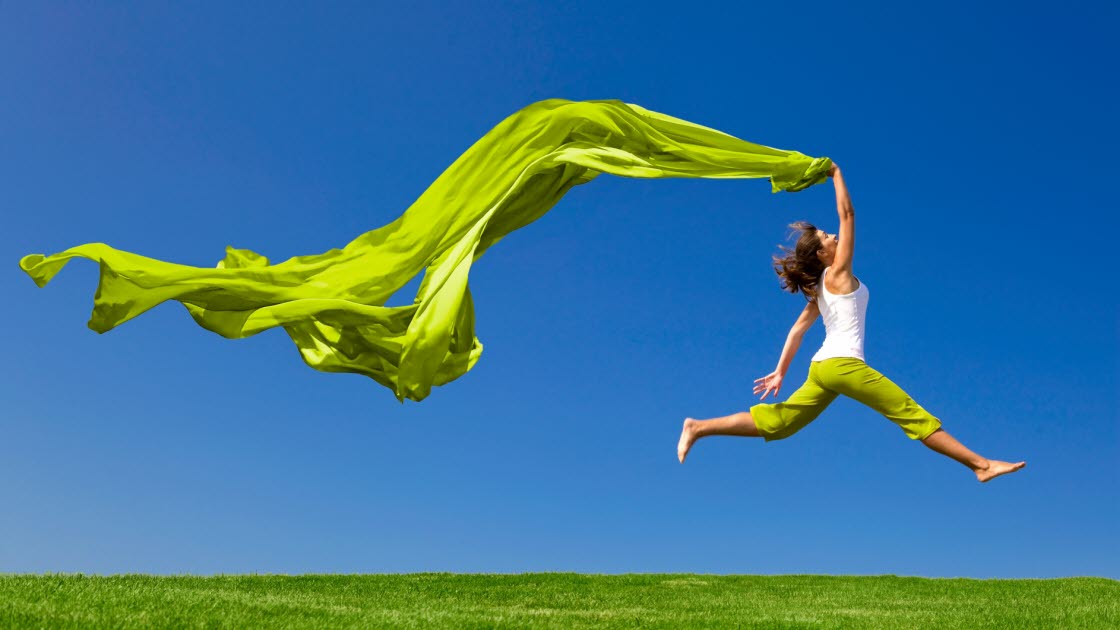 Ung kvinna hoppar på en grön äng med en färgade tyger.